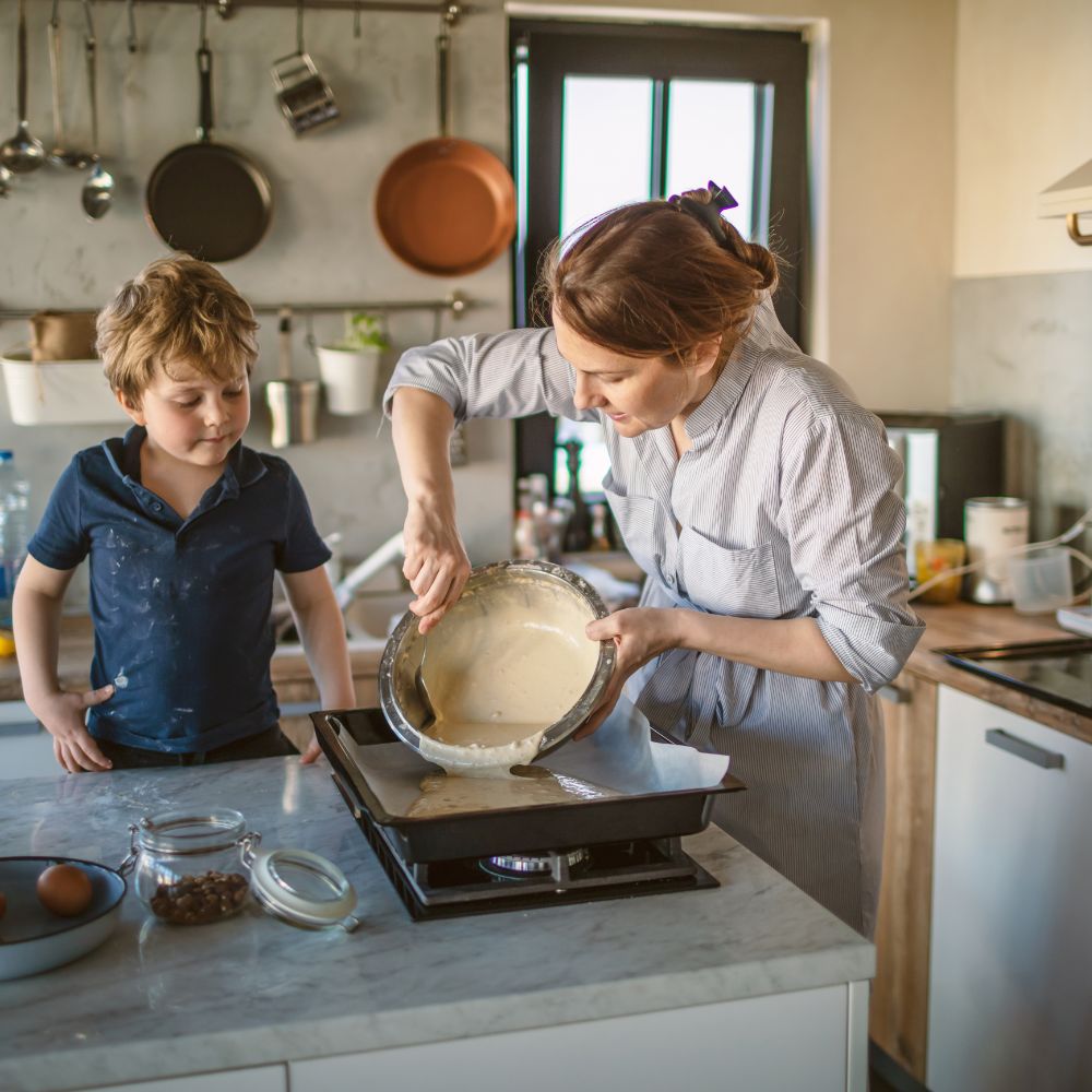 A loving mother and her young son baking together in a warm home kitchen, sharing a creative bonding moment surrounded by ingredients and joy.
