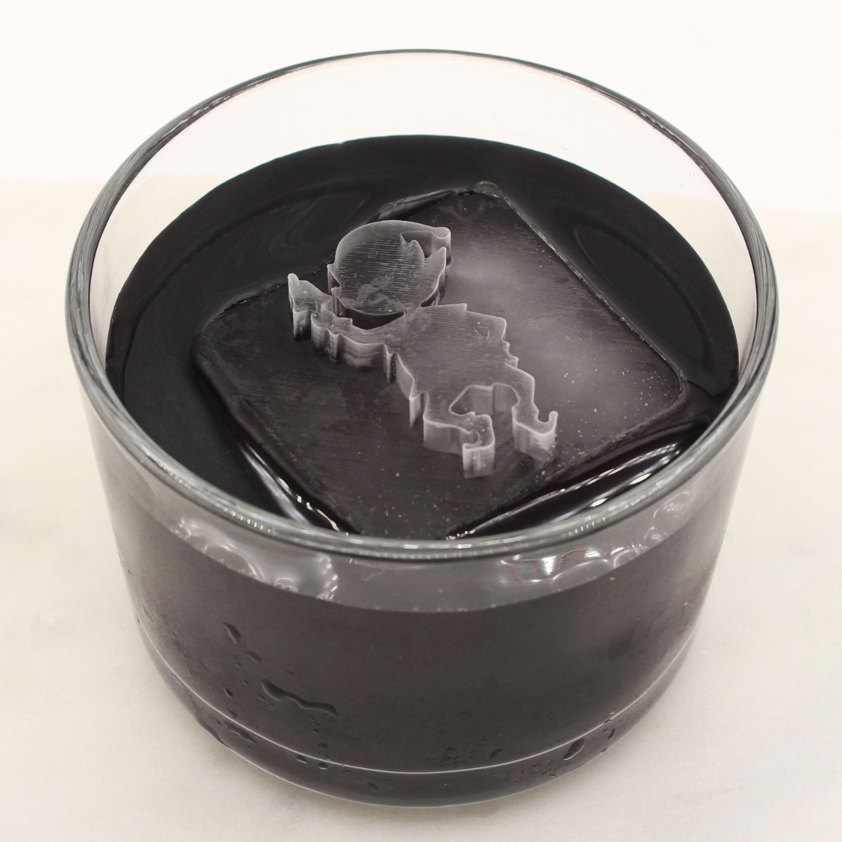 Large elf-shaped ice cube floating in a dark holiday cocktail, adding playful festive character to the drink.