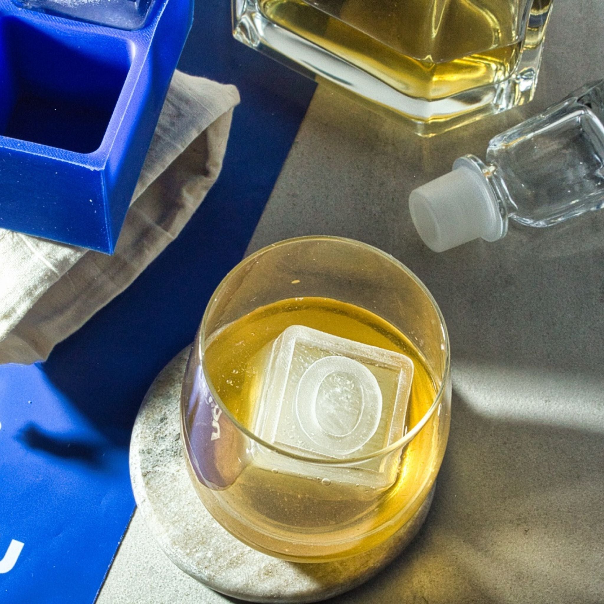 Clear monogrammed O ice cube served in whiskey glass, styled with custom blue tray in background