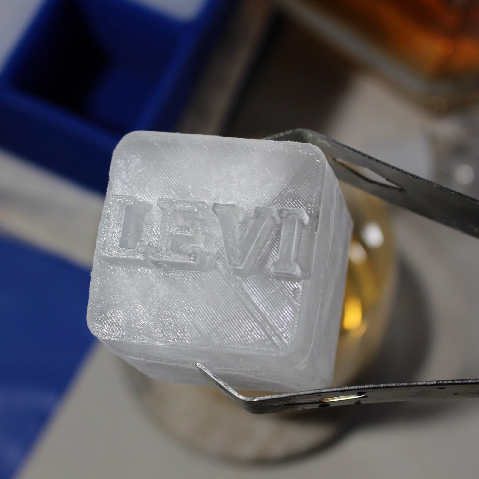 Frosted personalised ice cube with "LEVI" text held by tongs, showing close-up engraving texture β great for birthdays or whiskey lovers