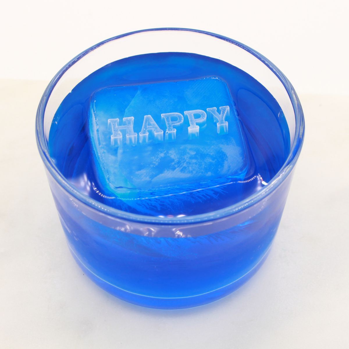 A raised “HAPPY” message ice cube floating in a bright blue drink, spreading positive energy with every sip.