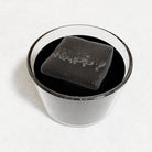 Personalised ice cube spelling HAPPY floating in a dark black drink, handmade platinum-silicone cube with raised letters by Chilled Out Creations.