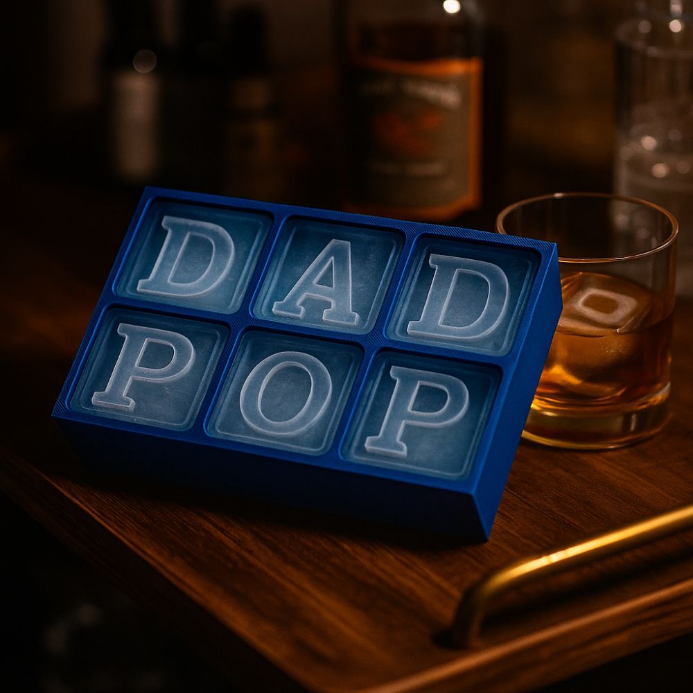 A custom blue ice tray filled with clear raised-letter ice cubes spelling DAD and POP, sitting on a bar cart beside a whiskey glass – perfect gift for cool dads.