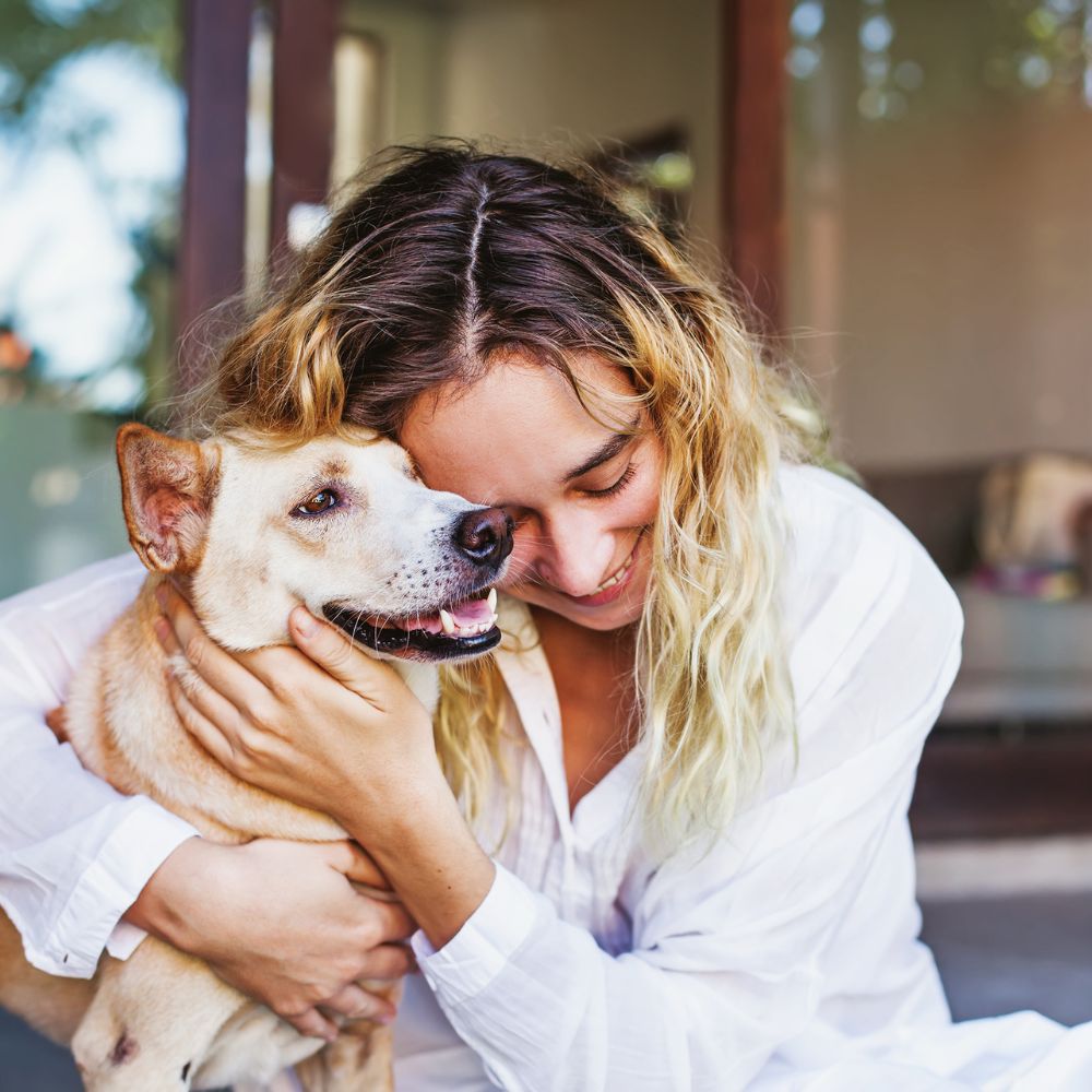 Woman in white shirt embracing her tan dog outside with eyes closed, expressing love and connection—ideal for personalised gifts for pet mums.