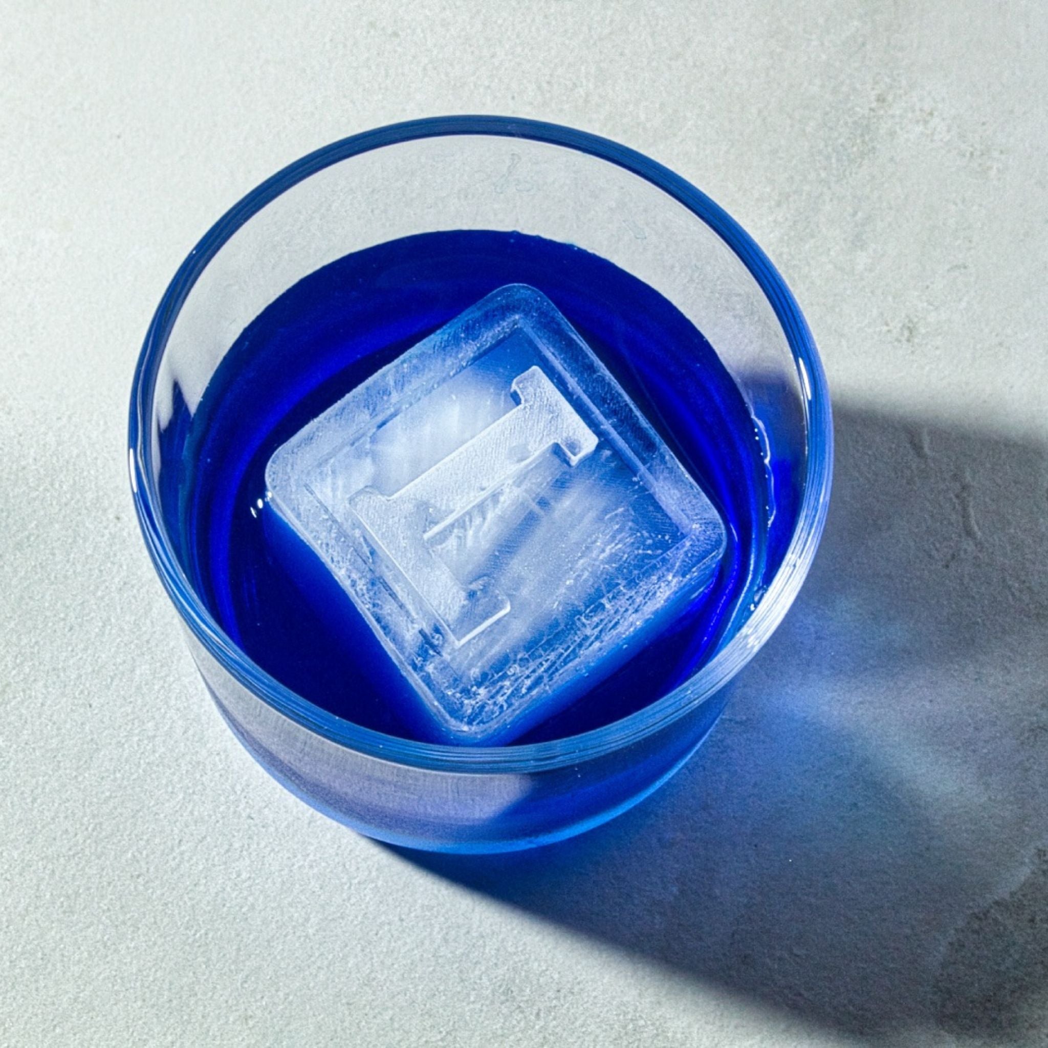 Monogrammed L ice cube floating in a bold blue cocktail, perfect for stylish events