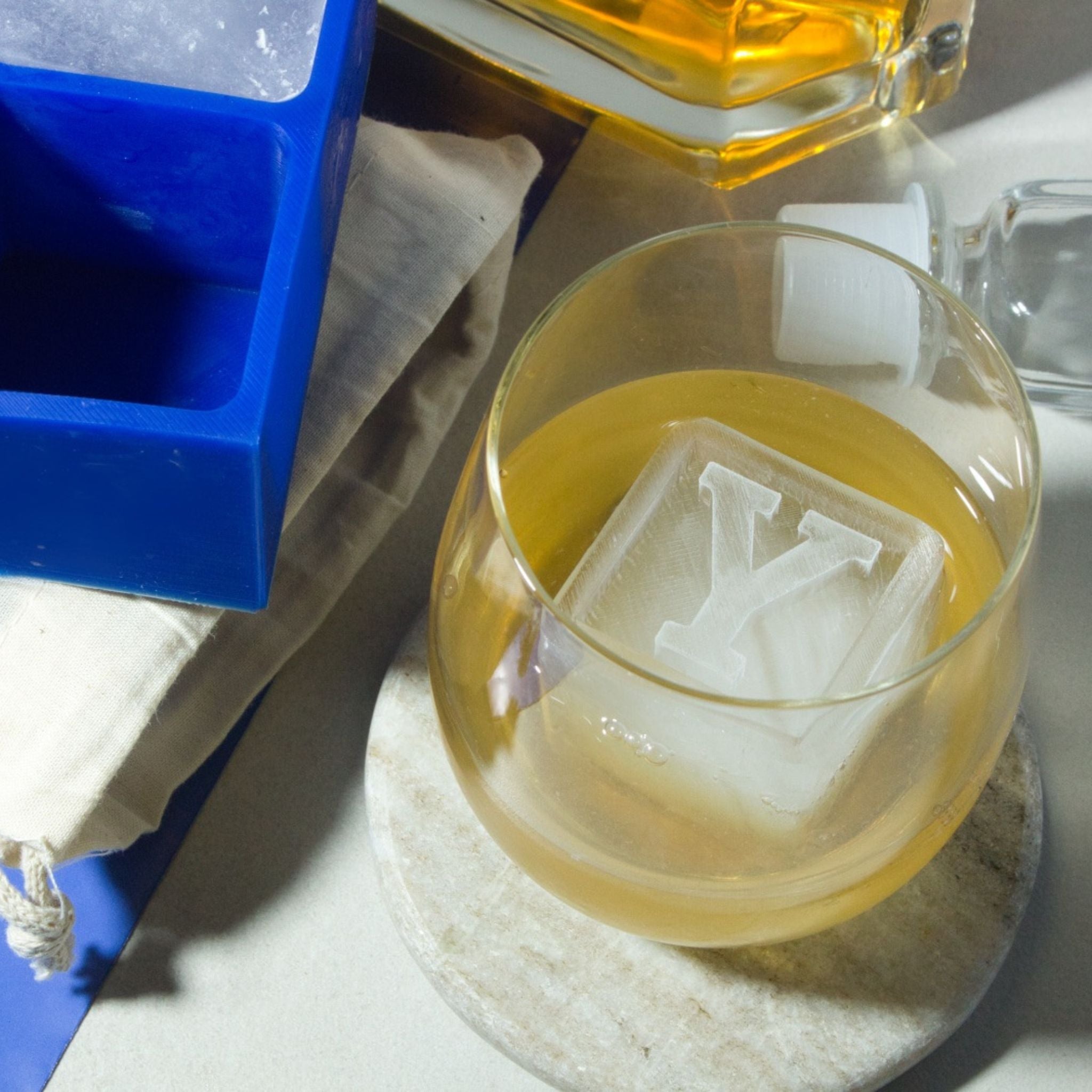 Hand-poured custom Y ice cube in a whiskey tumbler, shown beside black tray and spirits for luxe gifting