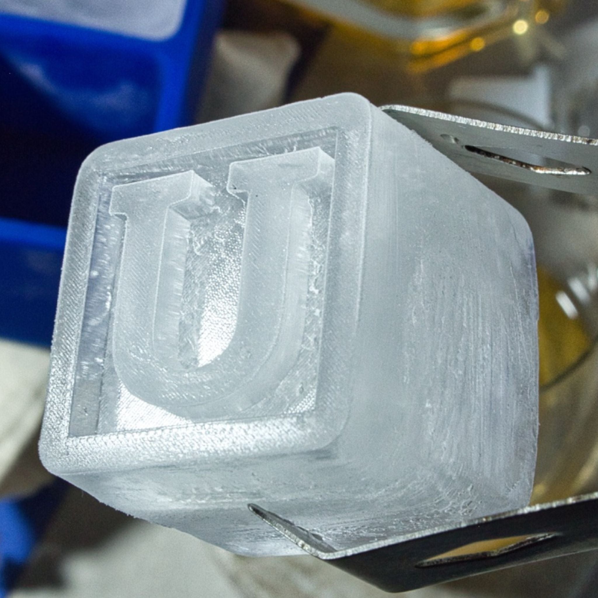 Frosty square ice cube with a bold U monogram held by tongs, close-up detail – an elegant option for custom birthday or anniversary presents, handmade in Australia.