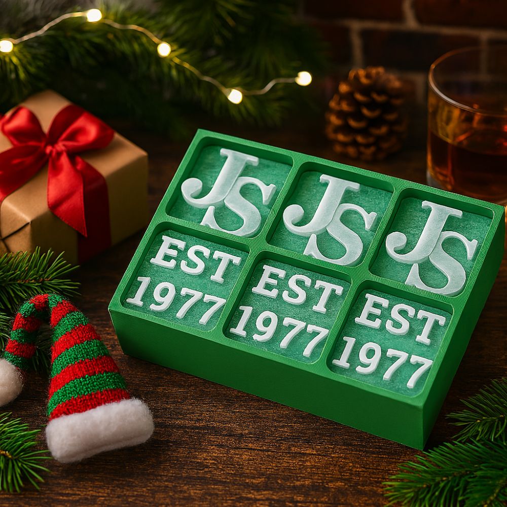 Custom green silicone ice tray with ‘JS EST 1977’ letters, styled on a festive wooden table with Christmas lights, pine branches, gift box and whisky glass – ideal personalised Christmas gift for men