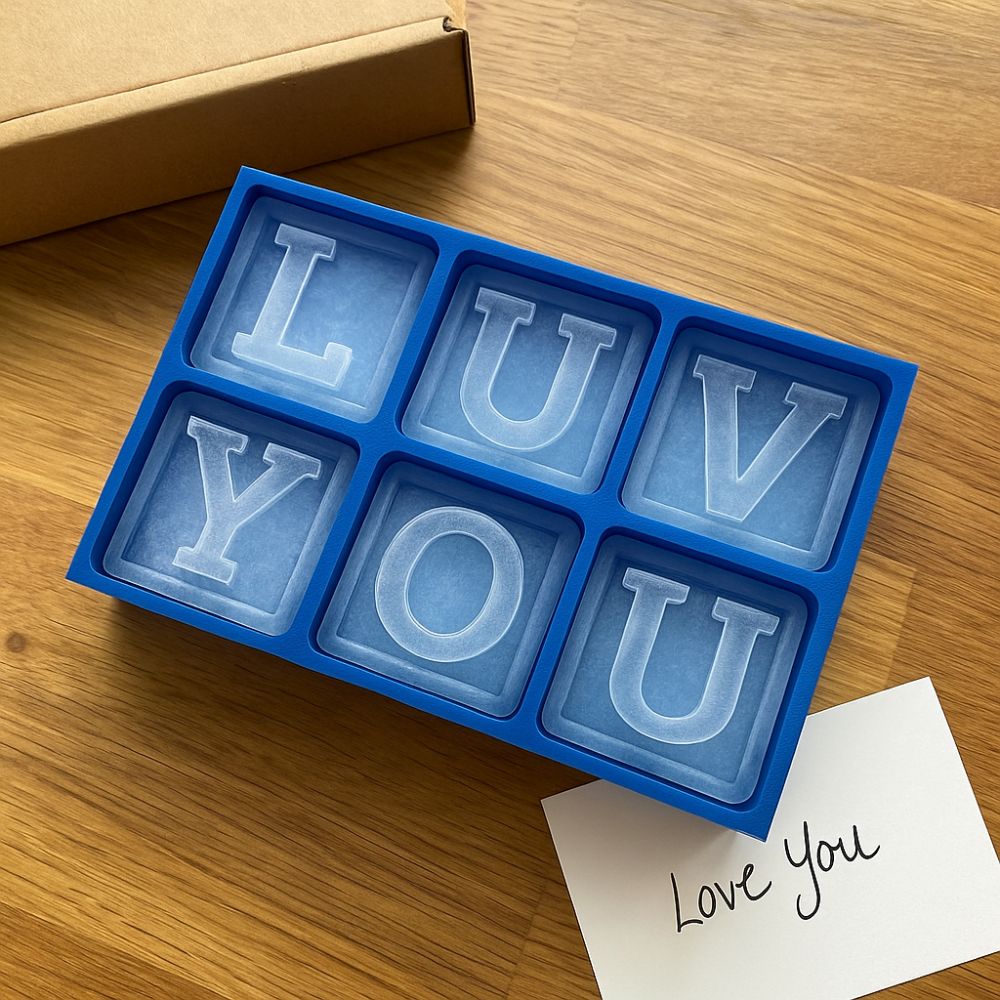 A bright blue custom ice tray spelling out “LUV YOU” on a timber bench, with a handwritten gift card reading “Love You” and eco-friendly packaging nearby — a heartfelt and affordable gift for boyfriends.