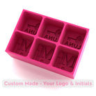 Vibrant pink silicone ice tray with raised logo and initials in each cube cavity, a playful yet stylish personalised gift option.