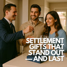 A professional real estate agent handing over house keys to a smiling young couple in their new modern home, while champagne glasses with clear square ice cubes and a premium gift box containing a 6-cube platinum silicone ice tray sit on the kitchen island, symbolising celebration and unique settlement gifting.