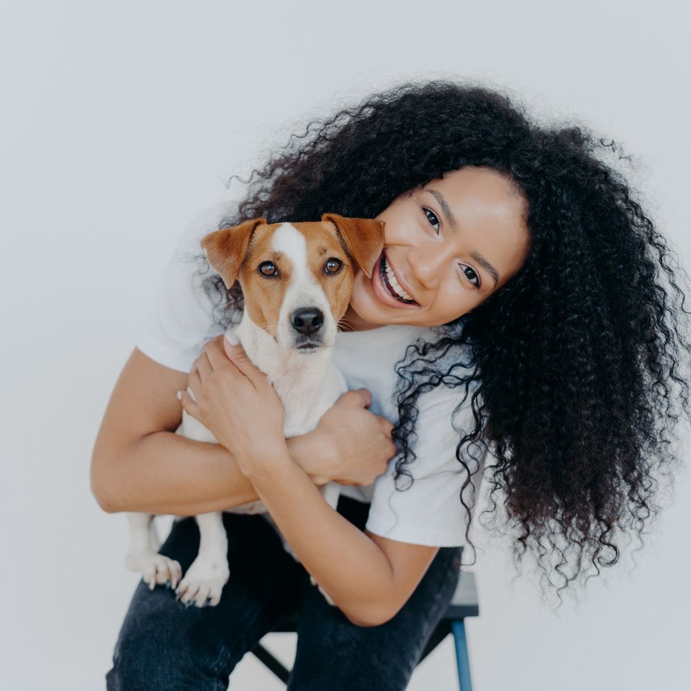 Smiling woman with curly hair hugging her Jack Russell terrier against a white background, capturing a joyful bond perfect for Gift for Pet Mum themes.