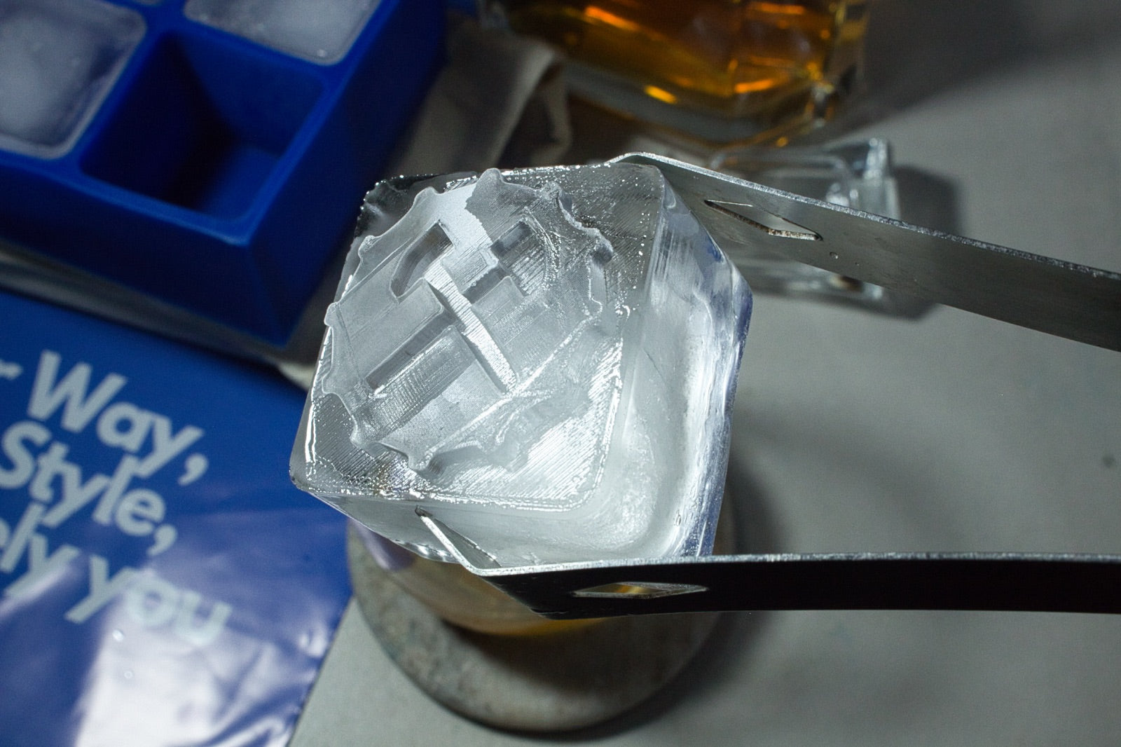 Close-up of a custom logo ice cube held with tongs, highlighting the precision and clarity of Chilled Out Creations' branded ice cube designs for corporate gifting and promotional use.