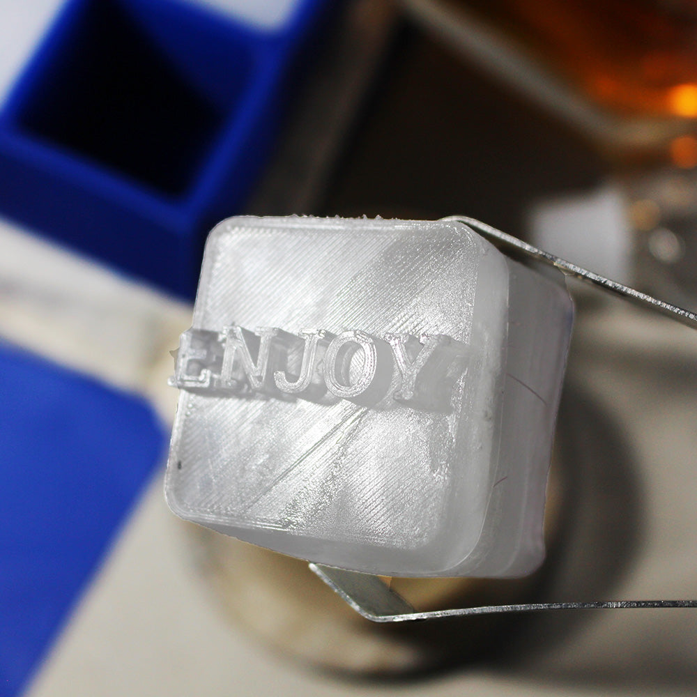 Personalised ENJOY ice cube held in metal tongs above a whiskey glass