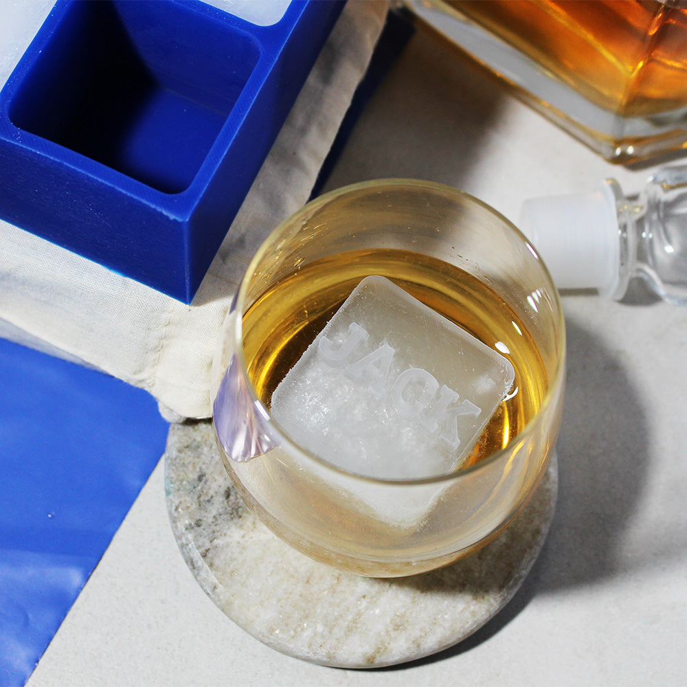 Engraved JACK ice cube in a whiskey glass beside a blue silicone ice tray