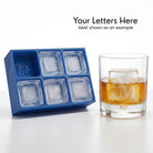 Blue A&M monogram silicone ice cube tray beside a whiskey glass holding a custom A&M engraved ice cube