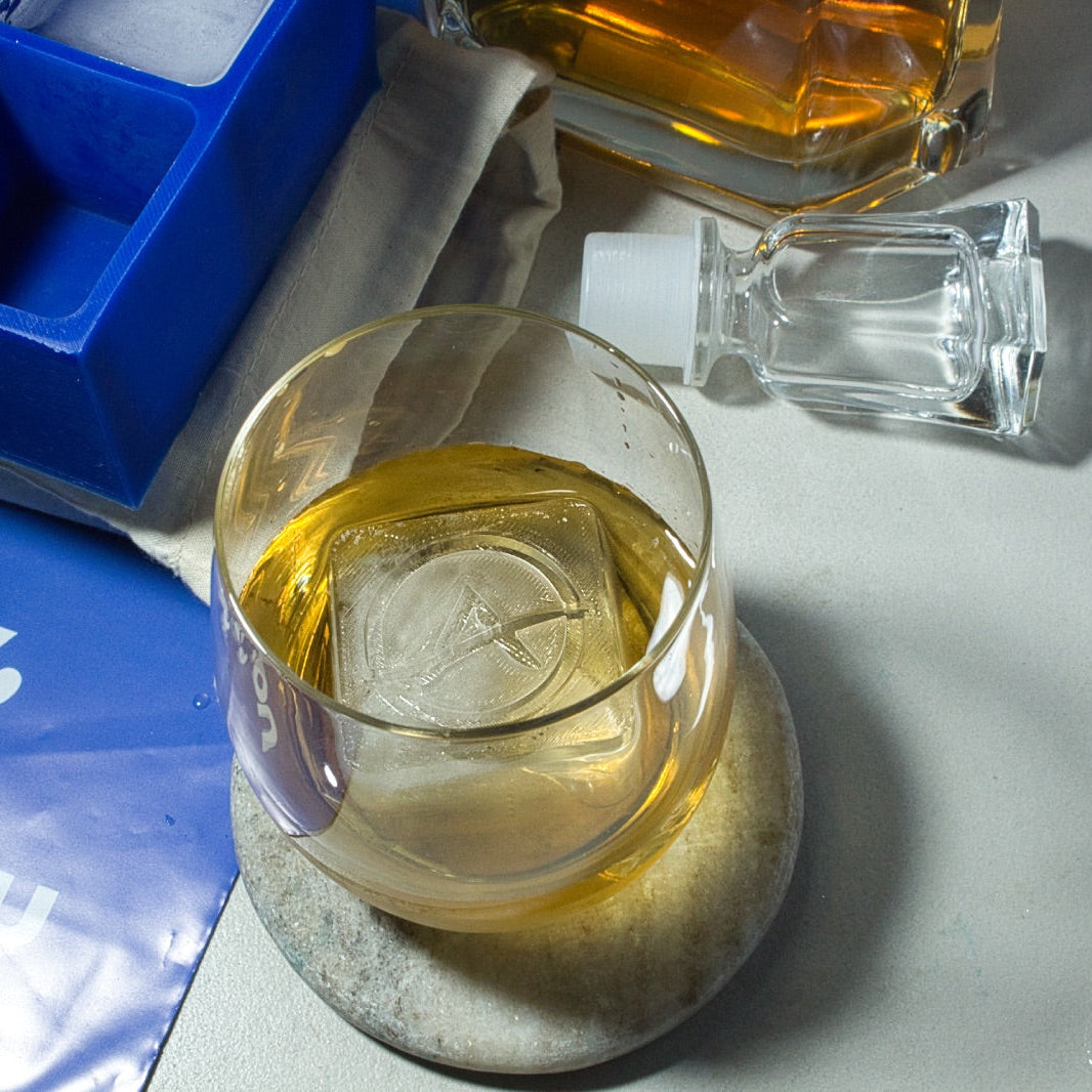 Personalised logo ice cube floating in a whiskey glass, next to a custom blue silicone tray – showcasing premium brand visibility in every sip.