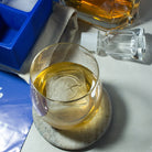 Personalised logo ice cube floating in a whiskey glass, next to a custom blue silicone tray – showcasing premium brand visibility in every sip.