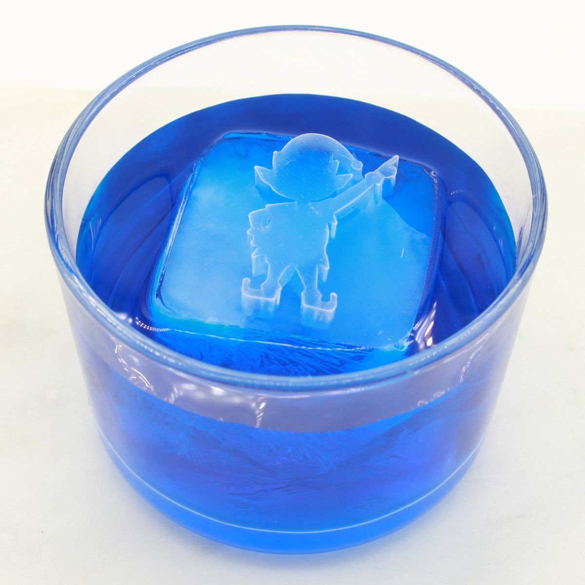 Blue cocktail showcasing a detailed elf-shaped ice cube, adding playful mischief to holiday drink presentations.