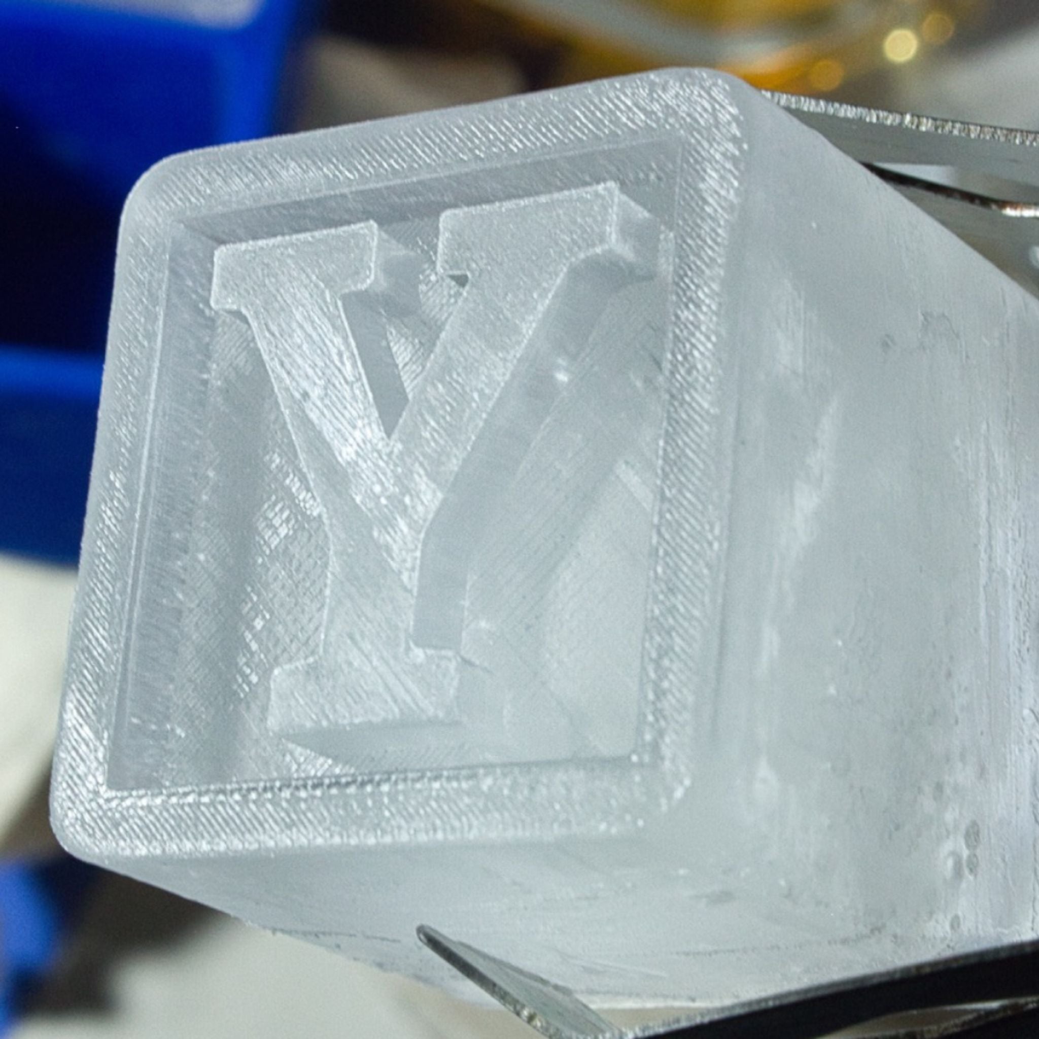 Detailed close-up of a monogrammed Y ice cube being lifted with tongs, showing crisp edges and luxury finish