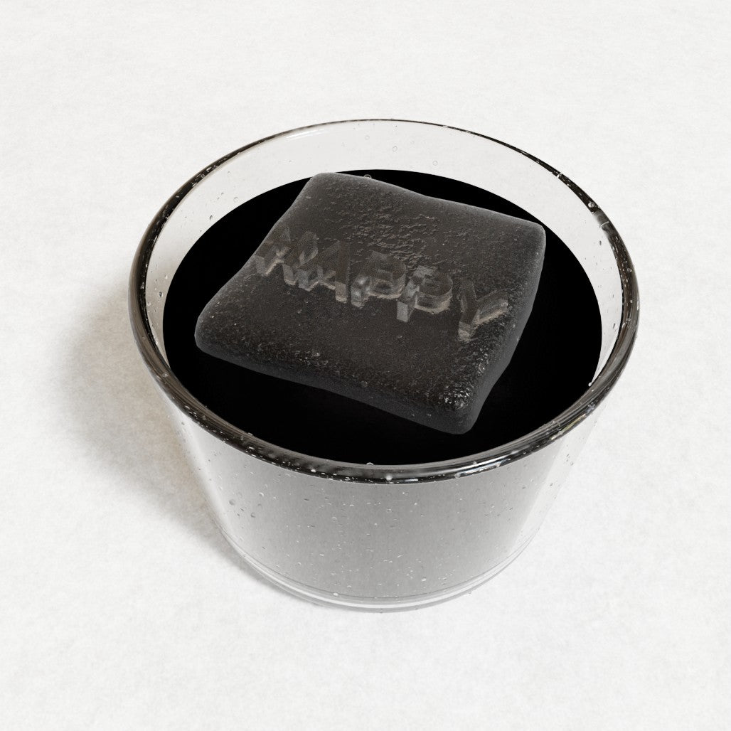 Personalised ice cube spelling HAPPY floating in a dark black drink, handmade platinum-silicone cube with raised letters by Chilled Out Creations.