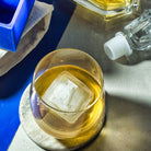 Close-up of clear L-shaped ice cube in a whiskey glass with bar tools in background