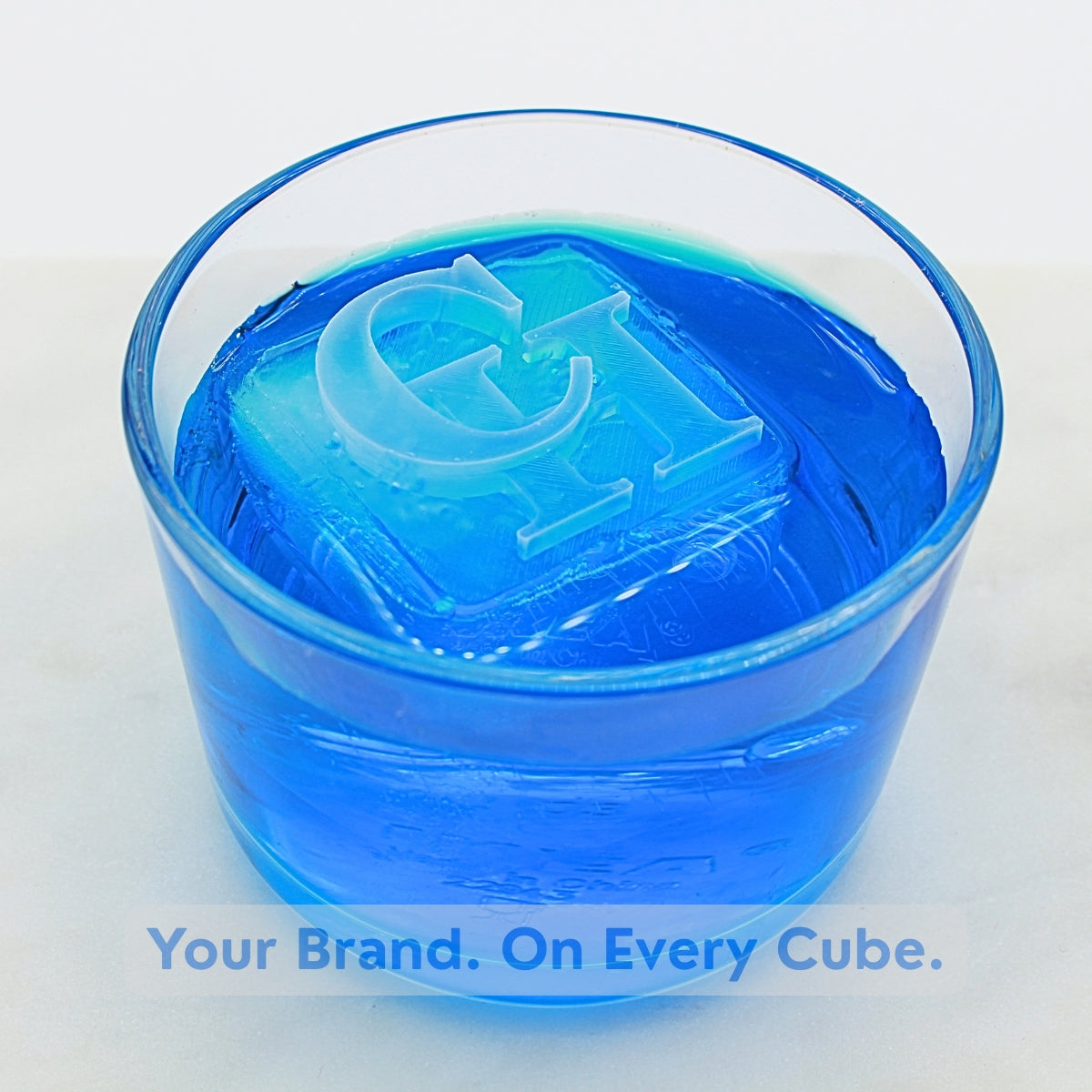 Blue drink with a large 45 mm ice cube featuring engraved initials, branded with “Your Brand. On Every Cube.” overlay, perfect for corporate gifting and client branding.