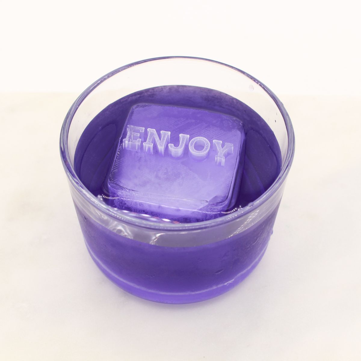 A cheerful purple drink featuring a clear ice cube engraved with “ENJOY,” made using a personalised message ice tray.