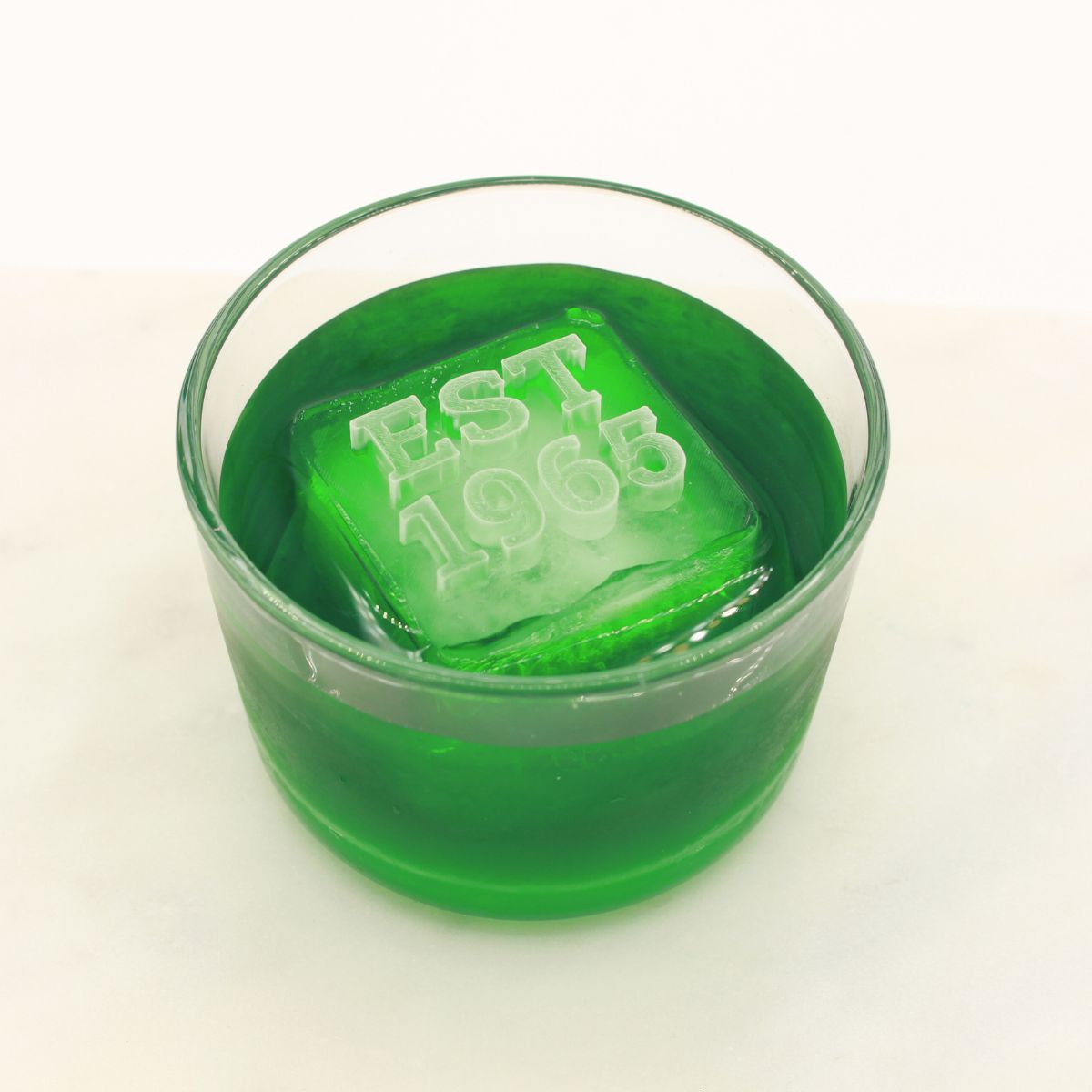 A vivid green drink showcasing an “EST 1965” ice cube, symbolising a birth year or anniversary in a custom silicone tray.