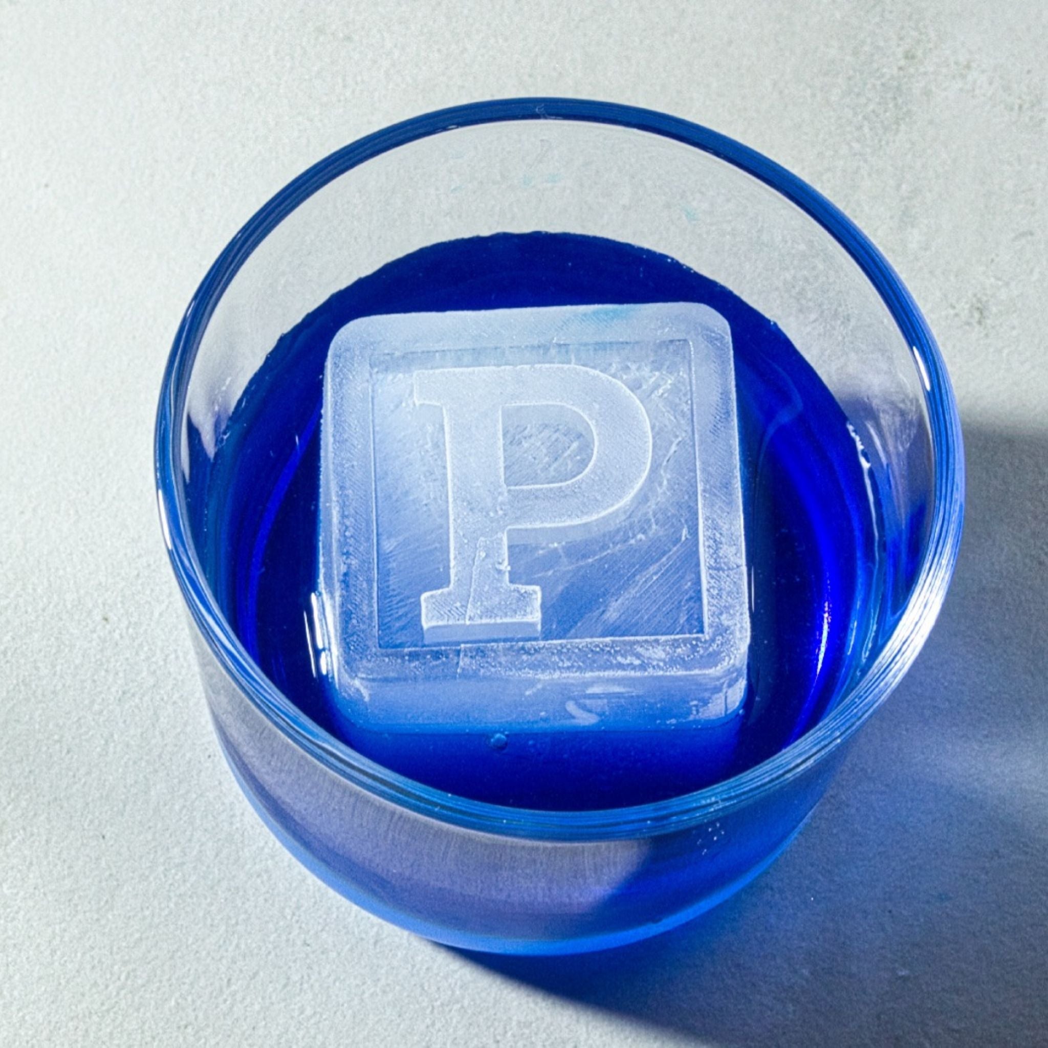 Custom P ice cube floating in a blue cocktail, showing off unique initial ice for unforgettable birthday parties or special occasions.