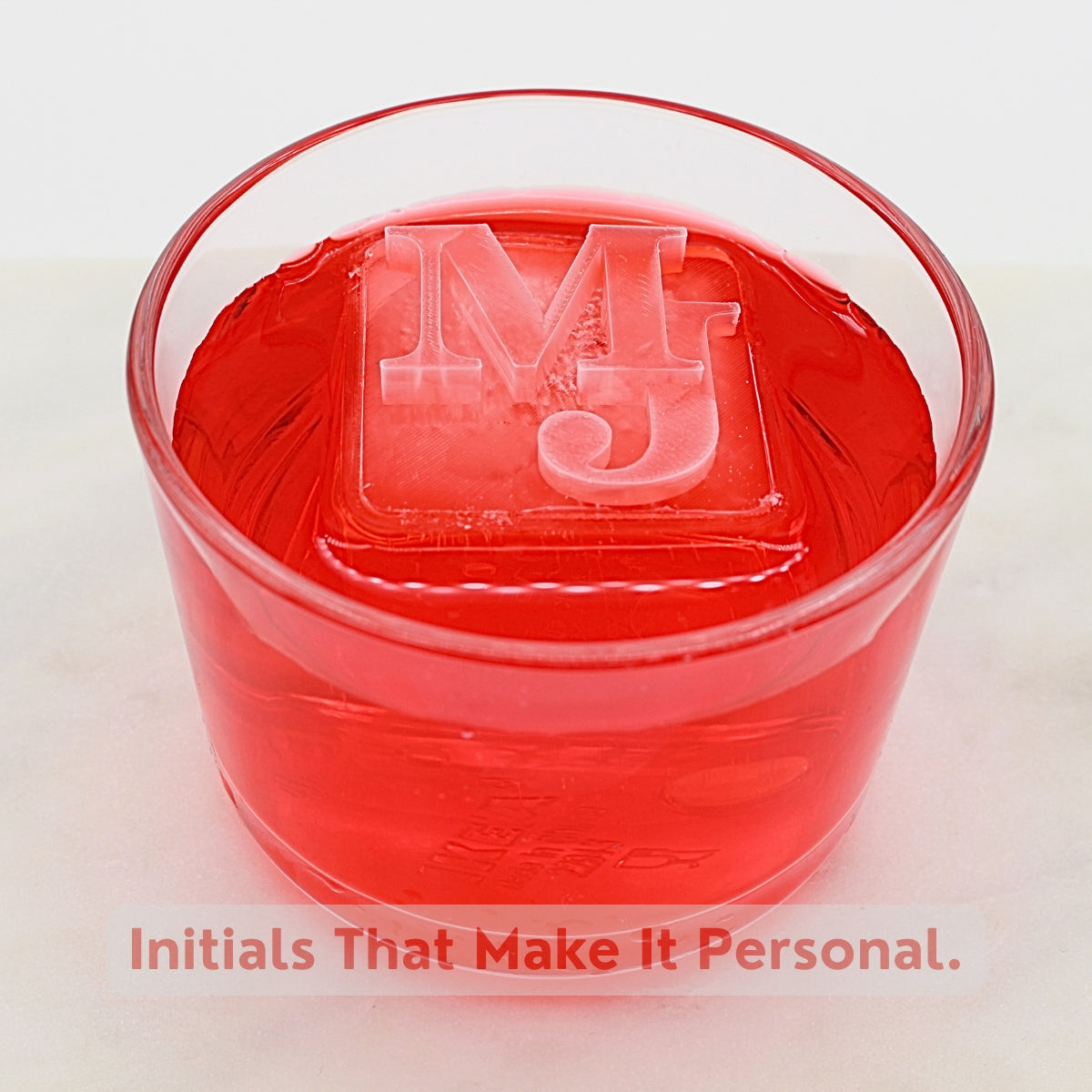 Bright red drink with a bold ice cube featuring custom initials, overlay text “Initials That Make It Personal,” designed for thoughtful corporate or client gifts.