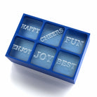 A royal-blue 6-cube silicone ice tray mould that creates raised words like HAPPY, CHEERS and JOY, designed for personal, meaningful drink moments.