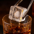 R&L Est 2025 monogrammed ice cube held with tongs above a whisky glass, showing the detailed initials