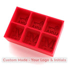 Bold red silicone ice tray moulding six custom cubes with initials and logo, designed as a unique gift or branded event accessory.