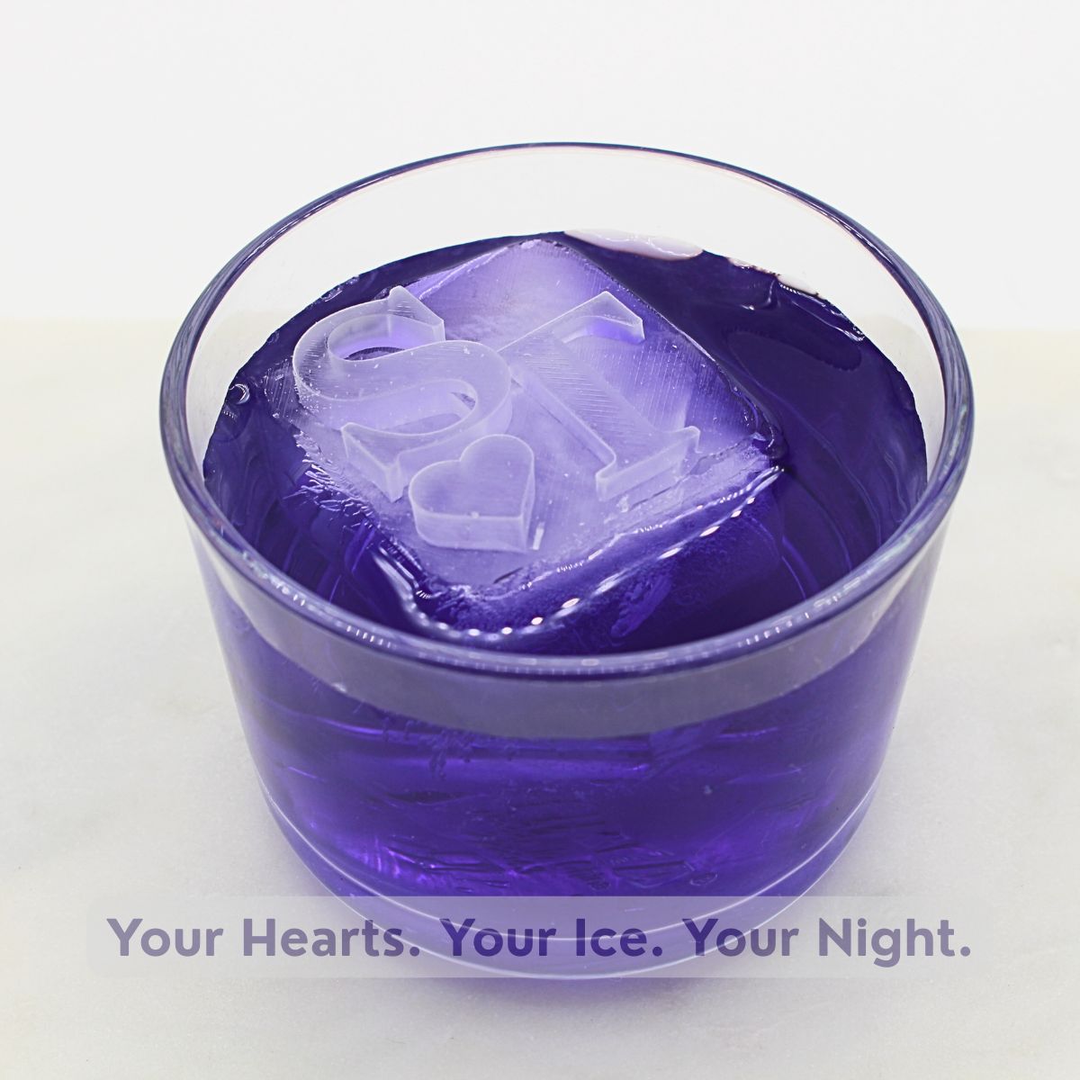 Close-up of a purple cocktail featuring a custom ice cube with raised heart and initials — perfect for couples’ celebrations.
