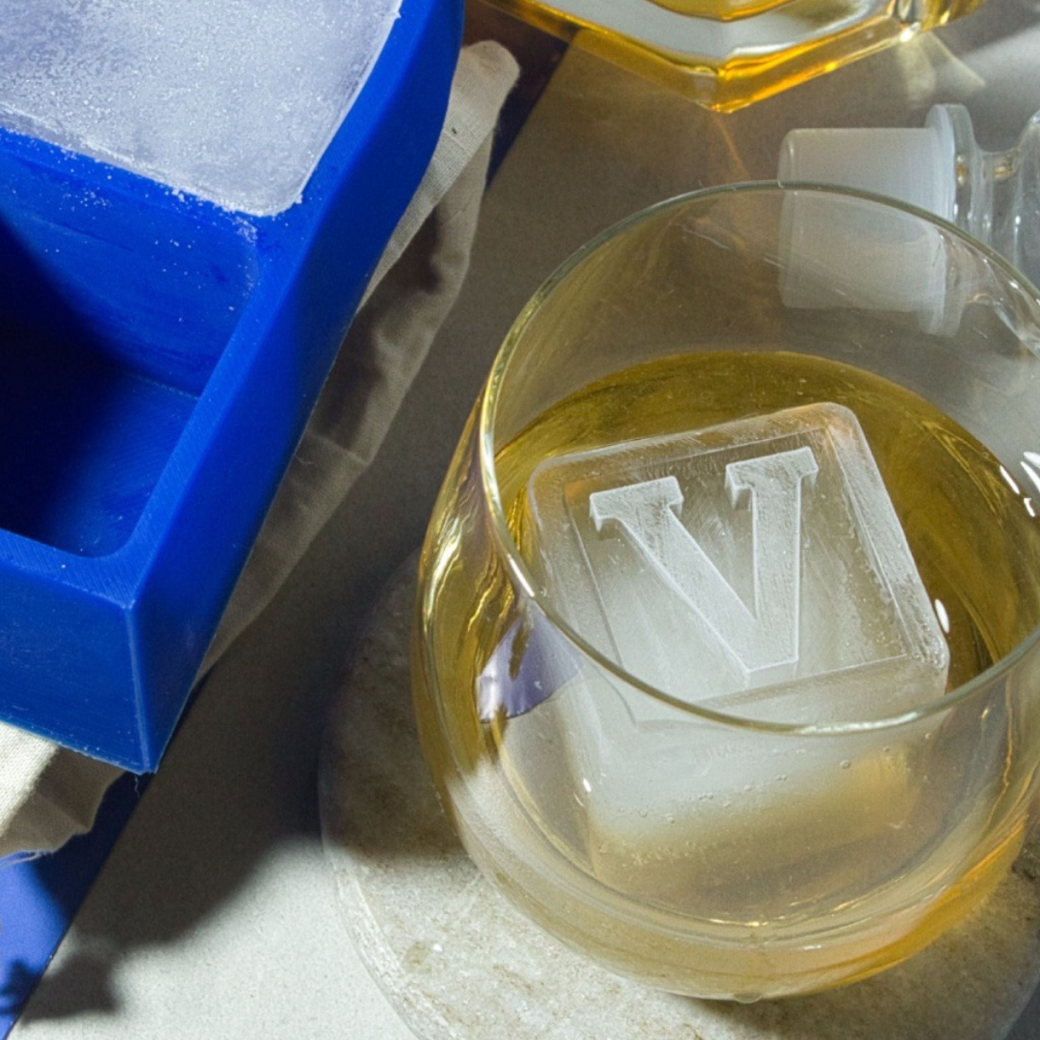 Monogrammed V ice cube in a whiskey glass, featuring custom blue tray in the background – perfect personalised gift for him.
