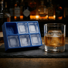 Blue Letter A ice tray beside a whiskey glass with a monogrammed A ice cube, moody bar background with bottles and candlelight