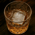 Close-up of a crystal whiskey glass with a large ice cube embossed with the letter A, warm ambient lighting