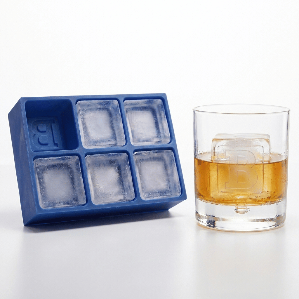 Blue Letter B ice tray next to a whiskey glass featuring a large B-embossed ice cube, bright natural light