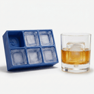 Blue silicone Letter G ice cube tray beside a rocks glass of amber whiskey chilled with a large clear ice cube stamped with the letter G, on a white background.