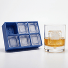 Blue silicone Letter H ice cube tray beside a rocks glass of amber whiskey chilled with a large clear ice cube stamped with the letter H, on a white background.