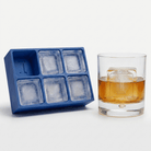 Blue silicone Letter I ice cube tray beside a rocks glass of amber whiskey chilled with a large clear ice cube stamped with the letter I, on a white background.