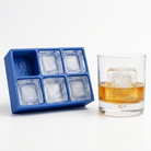Blue silicone Letter N ice cube tray beside a rocks glass of amber whiskey chilled with a large clear ice cube stamped with the letter N, on a white background.