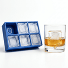 Blue silicone Letter O ice cube tray beside a rocks glass of amber whiskey chilled with a large clear ice cube stamped with the letter O, on a white background.