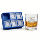 Blue silicone Letter Q ice cube tray beside a rocks glass of amber whiskey chilled with a large clear ice cube stamped with the letter Q, on a white background.