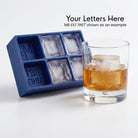 Personalised monogrammed ice cube in a whiskey glass beside the blue silicone tray
