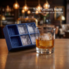 Blue monogrammed ice cube tray with personalised whiskey ice cubes served in a glass at a bar